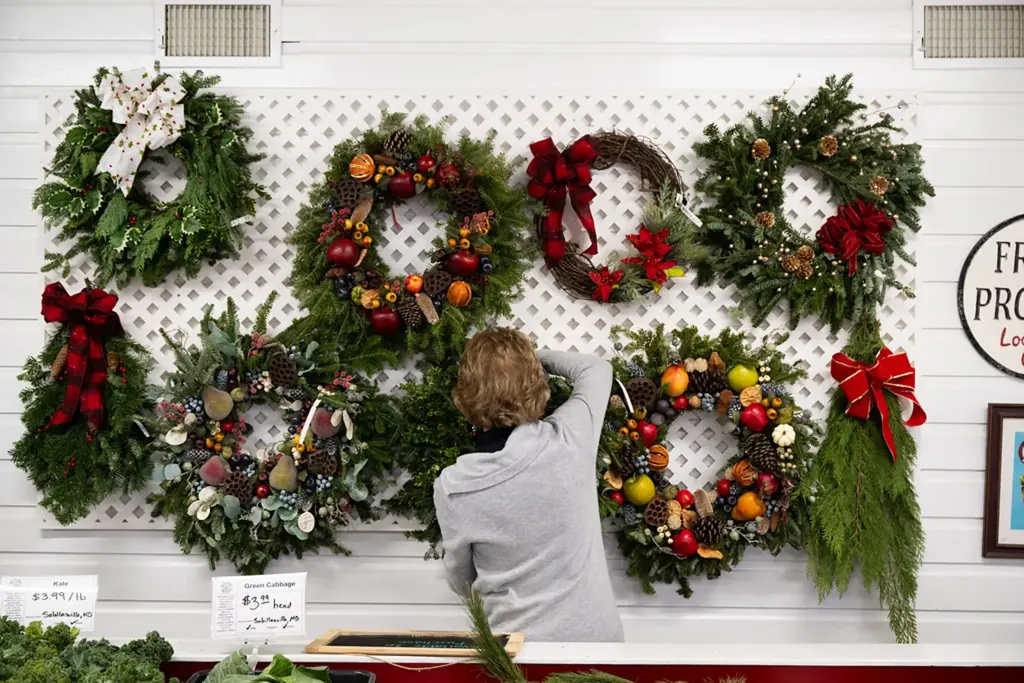A wall of handmade evergreen wreaths hanging in a farm shop while a worker hangs another.